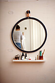 Round wall mirror with rope frame above floating shelf in bathroom