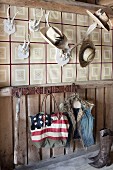 Stars and stripes bag and waistcoat hanging from wall hooks below various hats on antlers on wallpapered wall