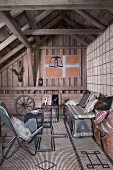 Butterfly armchair and bench with cushions on patterned sisal rug in rustic attic room with exposed wooden roof structure