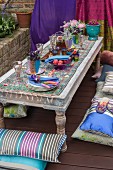 Low garden table with Indian-style table setting with coloured glasses and flowers and floor cushions on wooden decks