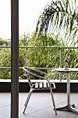 Blick auf Balkon mit Stuhl aus Metall und Holzleisten mit passendem Tisch, im Hintergrund Palmen
