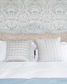 Cane headboard of bed with wooden frame against leaf-patterned wallpaper