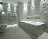 Bathtub, toilet and shower area in designer bathroom with marble tiles and 3D structured tiles