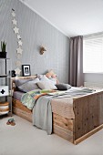 Collection of scatter cushions on rustic wooden bed against wallpapered wall