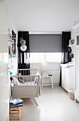 Retro cot, changing cabinet, grey roller blind and black curtains in nursery