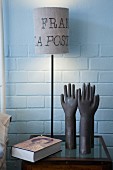 Table lamp with lettering on lampshade and hand-shaped ornaments on small bedside table