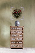 Vintage chest of drawers with fronts covered in wallpaper below decoupage picture applied to wall