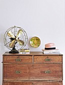 Old table-top fan on top of antique wooden chest of drawers