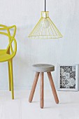 Stool with concrete seat and wooden legs below yellow pendant lamp
