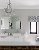 White, modern washstand with twin sinks, mirrored cabinet and half-height, exposed brick wall in modern, country-style bathrom