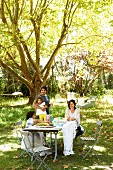 Family in sunny, summery garden around set table under shady tree