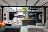 Sofas in open-plan interior with double-height dining area and steel staircase