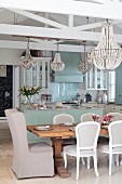 Chandelier above dining set with Rococo-style chairs around solid wood table in front of open-plan kitchen
