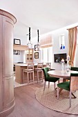 Dining table and chairs with green upholstery on round rug in front of island counter and bar stools made from pale wood