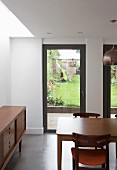 Dining area next to fifties-style, wooden sideboard; terrace doors with view of garden in background