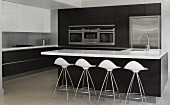 Designer bar stools with white shell seats at island counter with black base unit in front of fitted cupboards with integrated kitchen appliances
