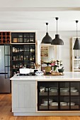 Island counter, charcoal pendant lamps and glass-fronted pantry cupboards in retro interior
