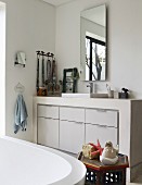 View across bathtub to masonry washstand with white fitted base cabinets