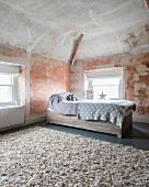 Child's bed with drawers below and pale grey blankets in purist, renovated attic room with patinated walls and ceiling