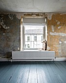 Soft toy and radiator in front of lattice window with Roman blind in room with patinated wall and blue-grey wooden floor
