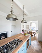 Vintage metal pendant lamps above free-standing kitchen counter with blue, patinated, country-house base units and oak worksurface