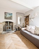 Sofa in front of log burner in old fireplace with antique mirror and stacked firewood in niches in comfortable lounge
