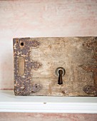 Rusty metal fittings on old piece of wood with keyhole against pale pink, patinated background