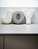Decorative fabric letters spelling 'JOY' on pale grey surface