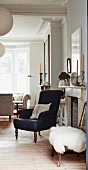 Black armchair and stool with white fur blanket next to open fireplace in traditional interior