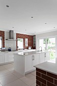 Open-plan kitchen with free-standing counter, white base units and long counter against brick wall