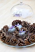Festive table centrepiece of pine cones & heart ornaments on glass plate in front off glass cover