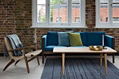 Classic-style armchair and wooden coffee table in front of sofa with blue cushions in loft-style interior
