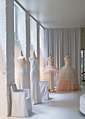 Elegant white dresses on tailors' dummies in white loft interior with floor-length curtains in background