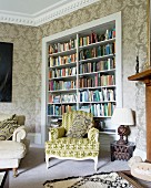 Rococo armchair with patterned upholstery in front of bookcase in niche in corner of traditional living room with ornate wallpaper
