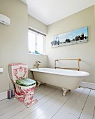 Ornate, antique toilet next to free-standing vintage bathtub on white-painted wooden floor of bathroom with walls painted pale grey