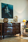 Table lamp on antique chest of drawers below portrait of woman on wall