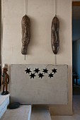 Zwei folkloristische Holzmasken an der Wand über einer Heizungsverkleidung mit Sternförmigen Ausschnitten