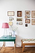 Table lamp on green side table and stool below framed pictures on wall