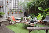 Old wooden bench and hand-made table in courtyard decorated with many potted plants and artificial grass rug