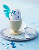 White egg decorated with blue rhinestones & feather in egg cup