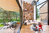 Loungeecke mit Klassikermöbel und raumhohem Bücherregal in zeitgenössischer Architektur, seitlich Blick auf Terrasse