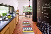 Open-plan kitchen with colourful rug on tiles floor and black wall painted with chalkboard paint