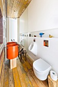 Modern bathroom with toilet, urinal and designer sink made from large, orange saucepan