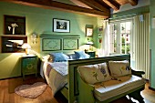Bemaltes Holzbett und Sitzbank in ländlichem Schlafzimmer mit grünen Wänden