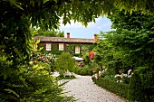 Blick durch Rankbogen auf Kiesweg und den romantisch angelegten Garten vor italienischem Landhaus