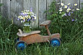 Campanula, ox-eye daisies and chamomile in jar on rustic, wooden push-along trike