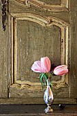 Pink tulips in silver vase in front of antique, carved cabinet door