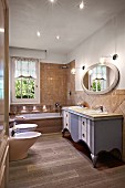Bad im Landhausstil mit graublau lackiertem Waschtisch, ovalem Wandspiegel, Badewanne, WC und Bidet