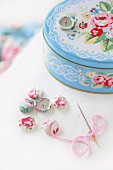 Romantic tin with pastel pattern of roses and lace, fabric-covered buttons and needle and thread
