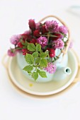 Small. white teapot holding posy of red clover flowers and raspberry leaves
